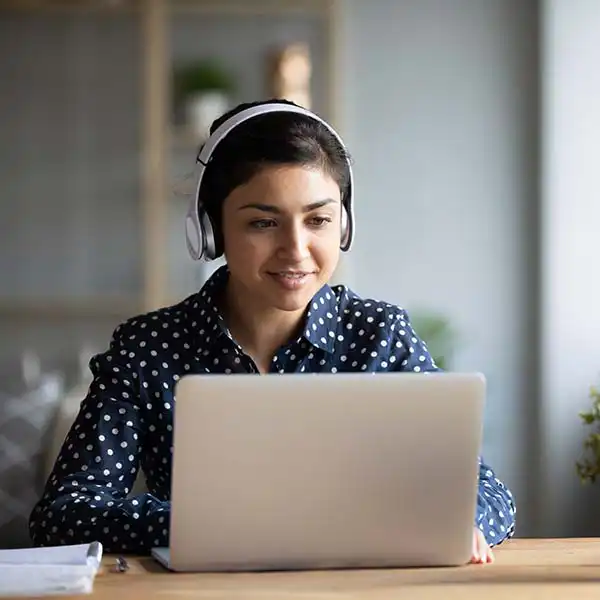 A woman wearing headphones and sitting at a desk with a laptop.